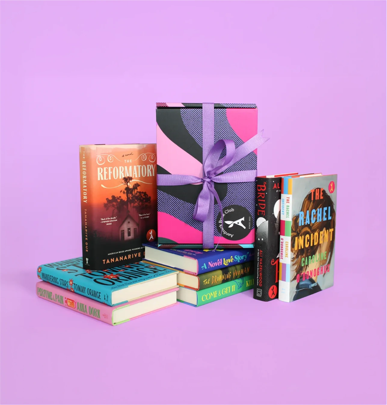Stack of colorful books with a pink and purple gift box tied with a lavender ribbon on a purple background.